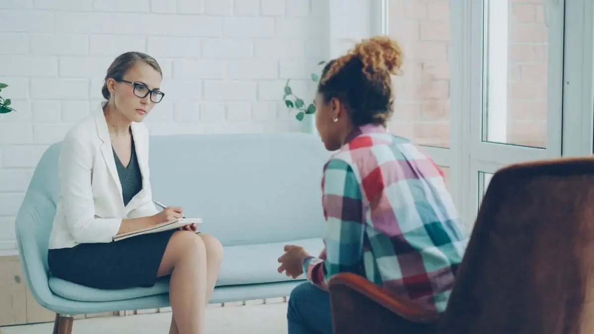 Therapist taking notes while talking with a client in a bright therapy office